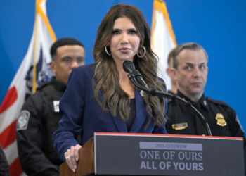 Homeland Security Secretary Kristi Noem drew backlash after a podium slogan at a press event was linked online to Nazi-era collective punishment rhetoric.