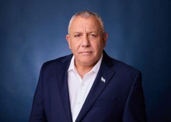Gadi Eisenkot, in a navy suit, white open-collar shirt and Israeli flag lapel pin, stands in front of a dark blue studio backdrop