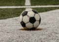 A worn black-and-white soccer ball resting on a painted spot on an artificial turf field