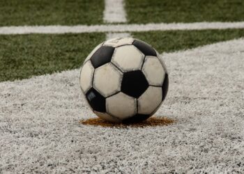 A worn black-and-white soccer ball resting on a painted spot on an artificial turf field