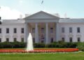 The north facade of the White House in Washington, with its columned portico, and a fountain on the North Lawn in front, on a clear day