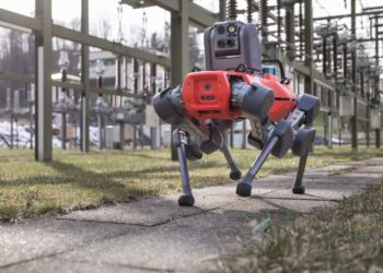 A gray and red ANYmal D four-legged robot walking through an electrical substation