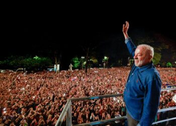 Luiz Inácio Lula da Silva raises his hand to a large nighttime crowd from a stage in São Paulo