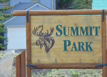 A wooden Summit Park sign with a carved moose head, in front of homes in Summit Park, Utah