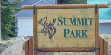 A wooden Summit Park sign with a carved moose head, in front of homes in Summit Park, Utah