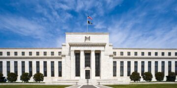 The white marble Eccles Building, headquarters of the Federal Reserve Board in Washington, under a blue sky with flags flying above the entrance