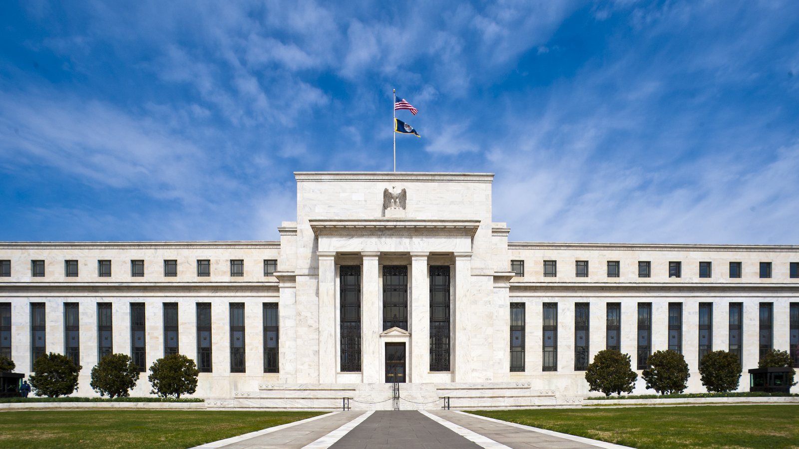 The white marble Eccles Building, headquarters of the Federal Reserve Board in Washington, under a blue sky with flags flying above the entrance