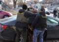 ICE officers in vests marked Police and ICE, seen from behind, escort a man to a car on a residential street in Chicago