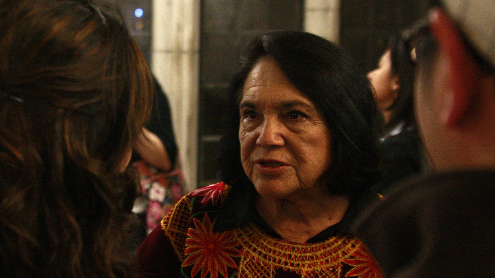 Dolores Huerta, in a dark blouse with red and gold embroidery, talks with students after a human rights keynote at the University of Chicago