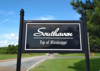 A black Southaven, Top of Mississippi city sign beside State Line Road, with cars on the road behind it