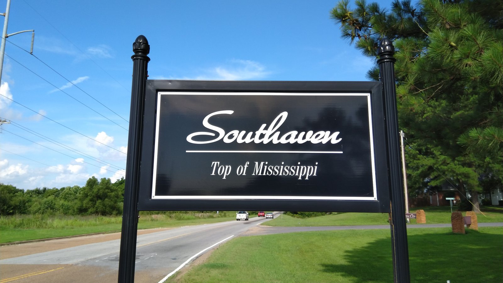 A black Southaven, Top of Mississippi city sign beside State Line Road, with cars on the road behind it
