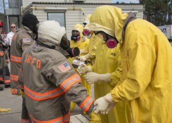 Savannah River Site firefighters in turnout gear and workers in yellow protective suits and respirators check equipment during a training drill