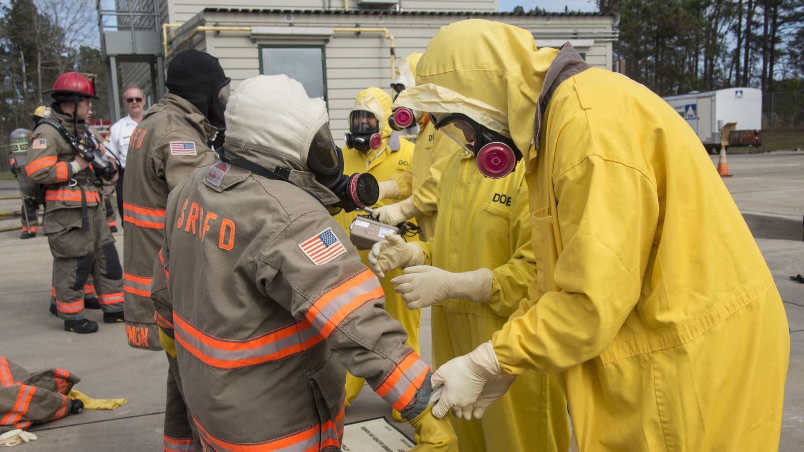 Savannah River Site firefighters in turnout gear and workers in yellow protective suits and respirators check equipment during a training drill