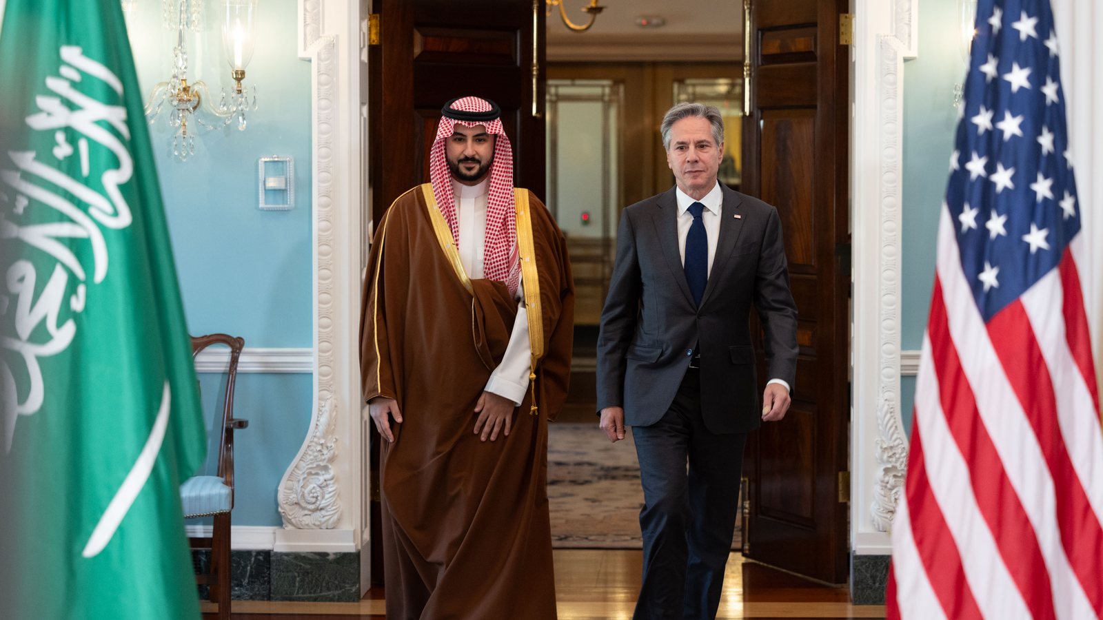 Saudi Defense Minister Prince Khalid bin Salman in a red-checked headdress and brown robe walks beside Antony Blinken at the State Department