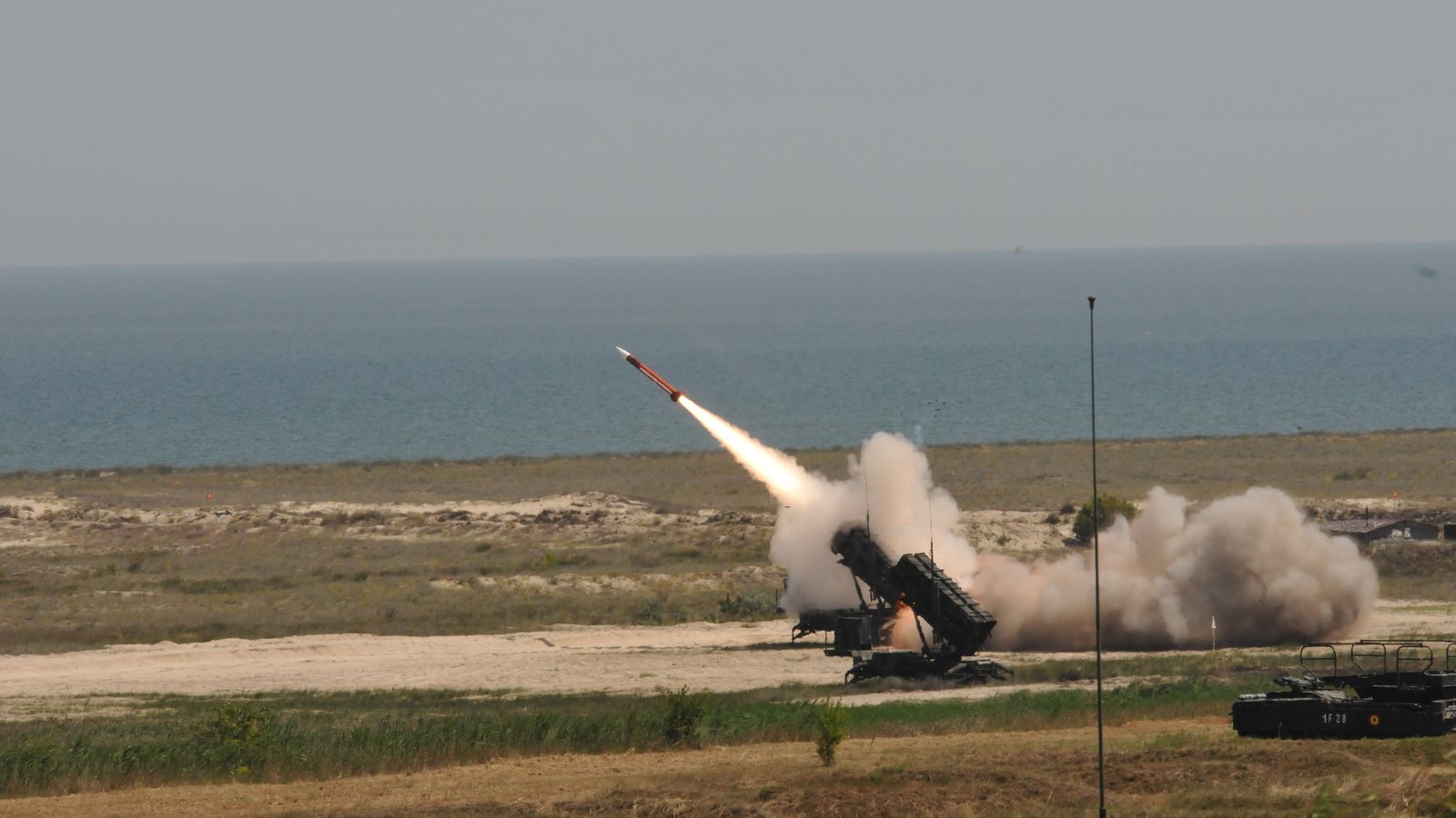 A US Army Patriot launcher fires a missile on a coastal range as smoke billows around it