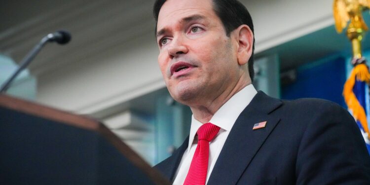Secretary of State Marco Rubio, in a dark suit and red tie, speaks at the White House briefing room podium