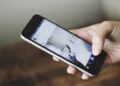 A hand holds a smartphone showing an Instagram feed, against a blurred background
