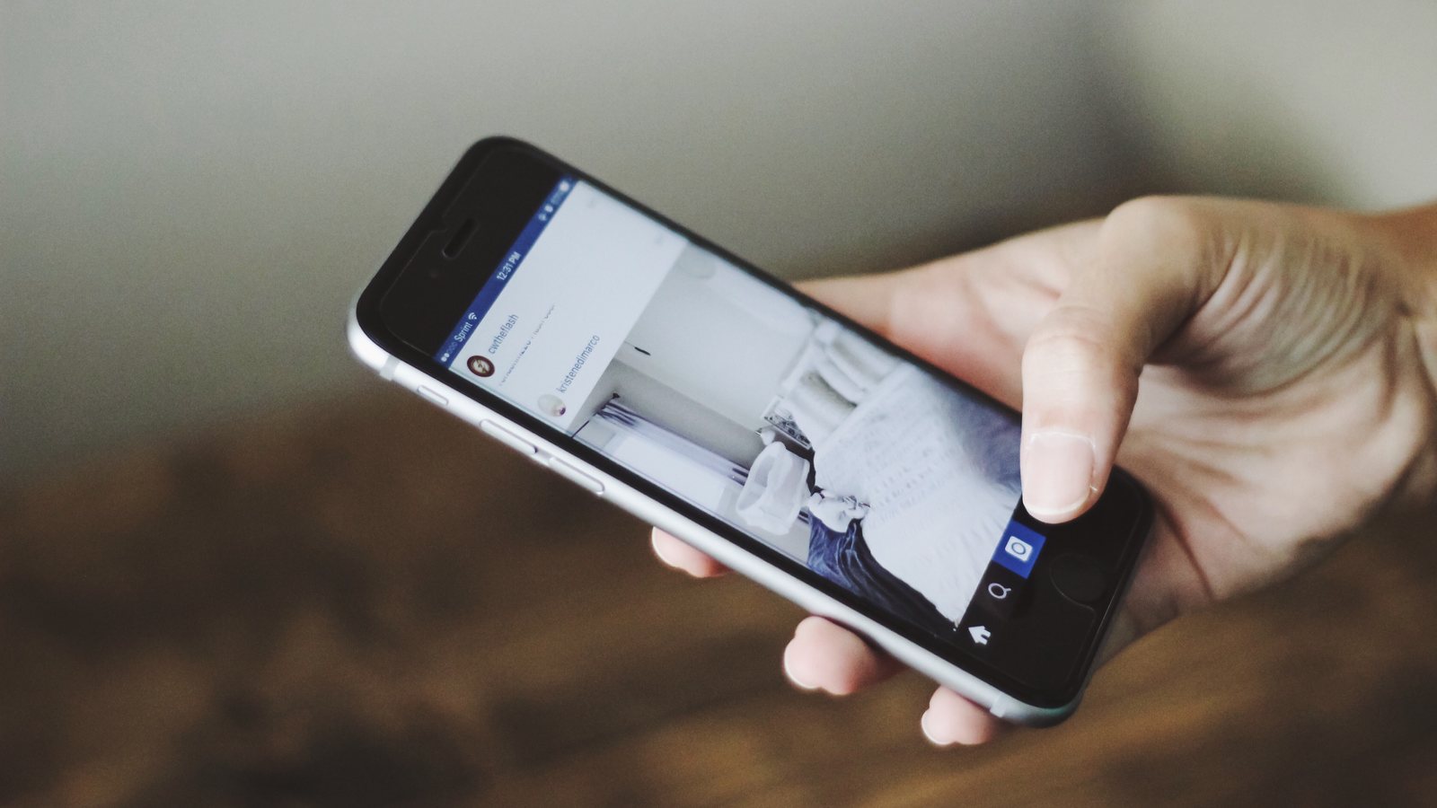 A hand holds a smartphone showing an Instagram feed, against a blurred background