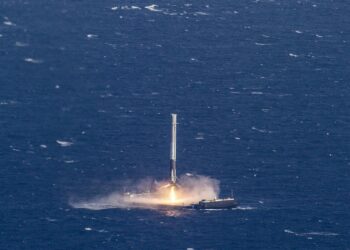 A rocket booster fires its engine as it lands upright on a drone ship in the open ocean