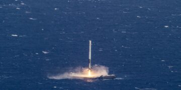 A rocket booster fires its engine as it lands upright on a drone ship in the open ocean