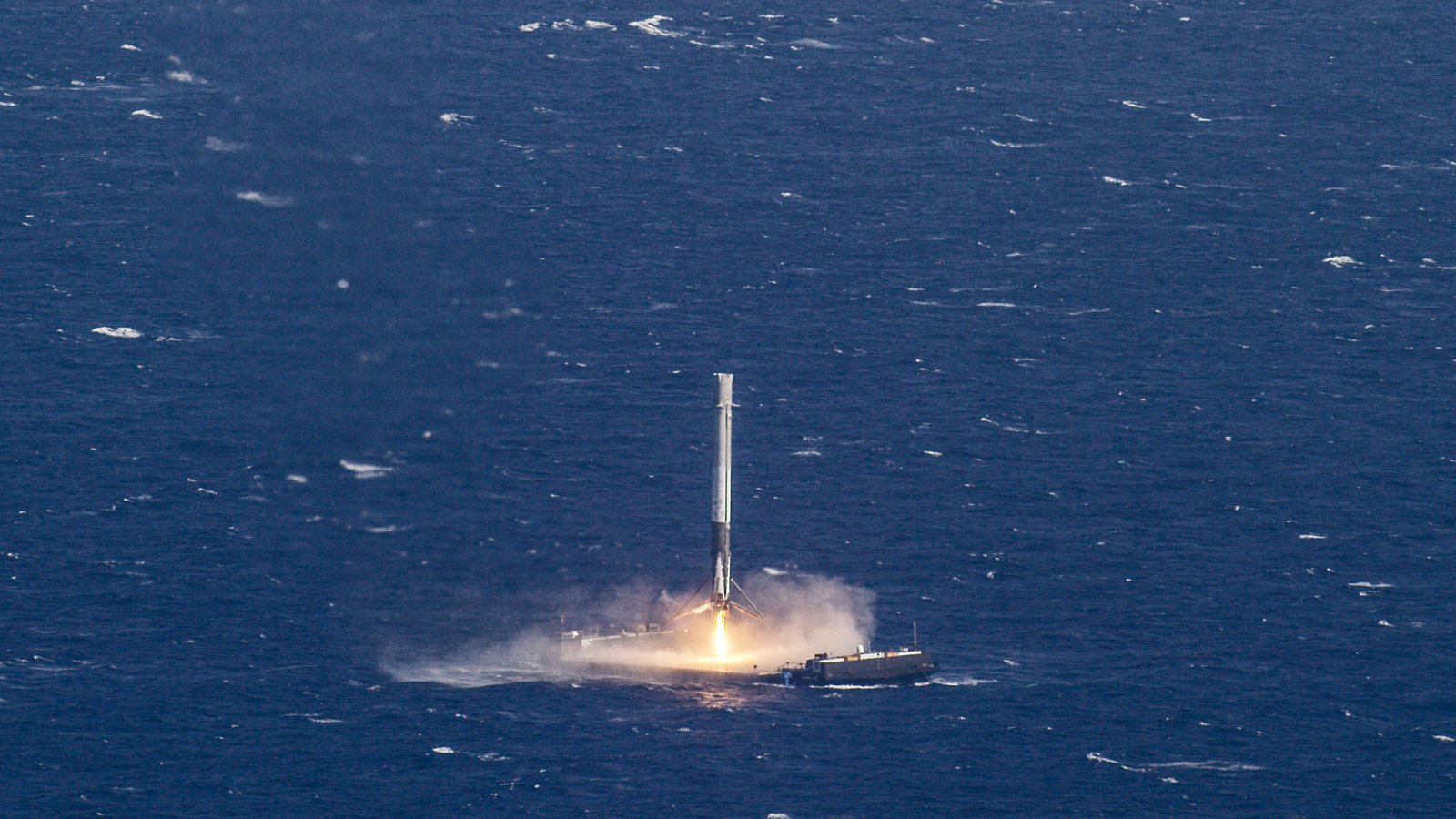 A rocket booster fires its engine as it lands upright on a drone ship in the open ocean
