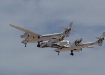 Virgin Galactic's twin-fuselage carrier aircraft Eve flying with an earlier SpaceShipTwo vehicle attached beneath it over Spaceport America