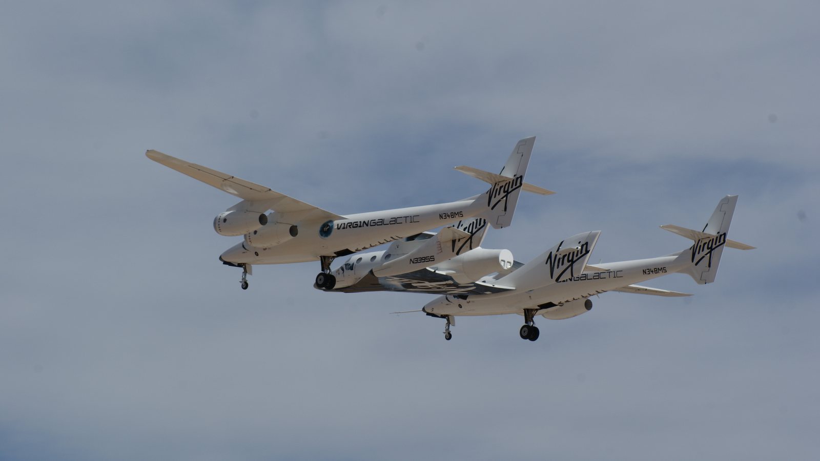 Virgin Galactic's twin-fuselage carrier aircraft Eve flying with an earlier SpaceShipTwo vehicle attached beneath it over Spaceport America
