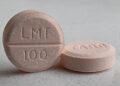 Two peach-colored generic lamotrigine tablets stamped LMT 100 on a gray countertop