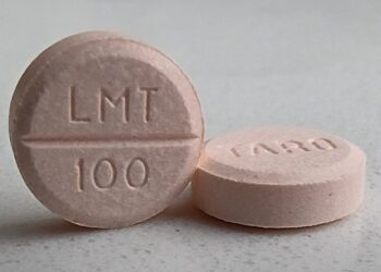 Two peach-colored generic lamotrigine tablets stamped LMT 100 on a gray countertop