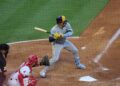 Brewers catcher William Contreras, in a gray road uniform and navy and gold helmet, watches a pitch from the batter's box as an Angels catcher and the umpire crouch behind the plate
