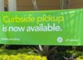 A green Publix and Instacart banner reading Curbside pickup is now available, hung above shrubs outside a store in West Miami