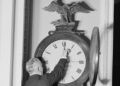 Senate Sergeant at Arms Charles Higgins reaches up to move the hands of the eagle-topped Ohio Clock in the US Capitol in 1918