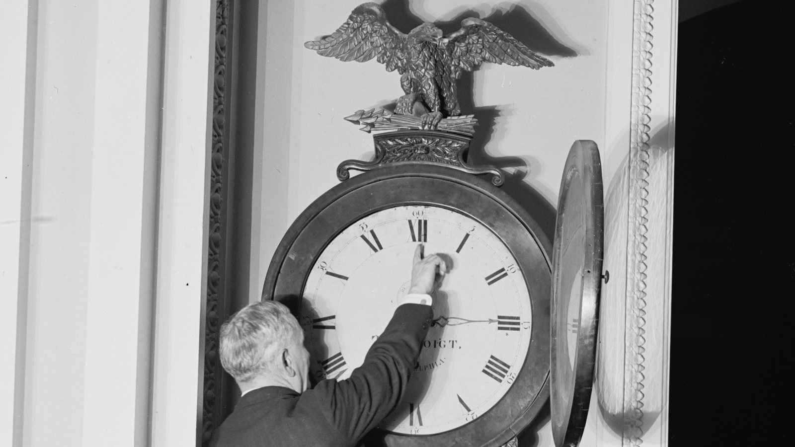 Senate Sergeant at Arms Charles Higgins reaches up to move the hands of the eagle-topped Ohio Clock in the US Capitol in 1918
