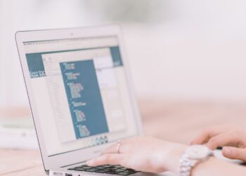 A person types on a laptop showing a code editor on a wooden desk
