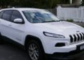 A white 2014 Jeep Cherokee parked on a residential street in front of a picket fence