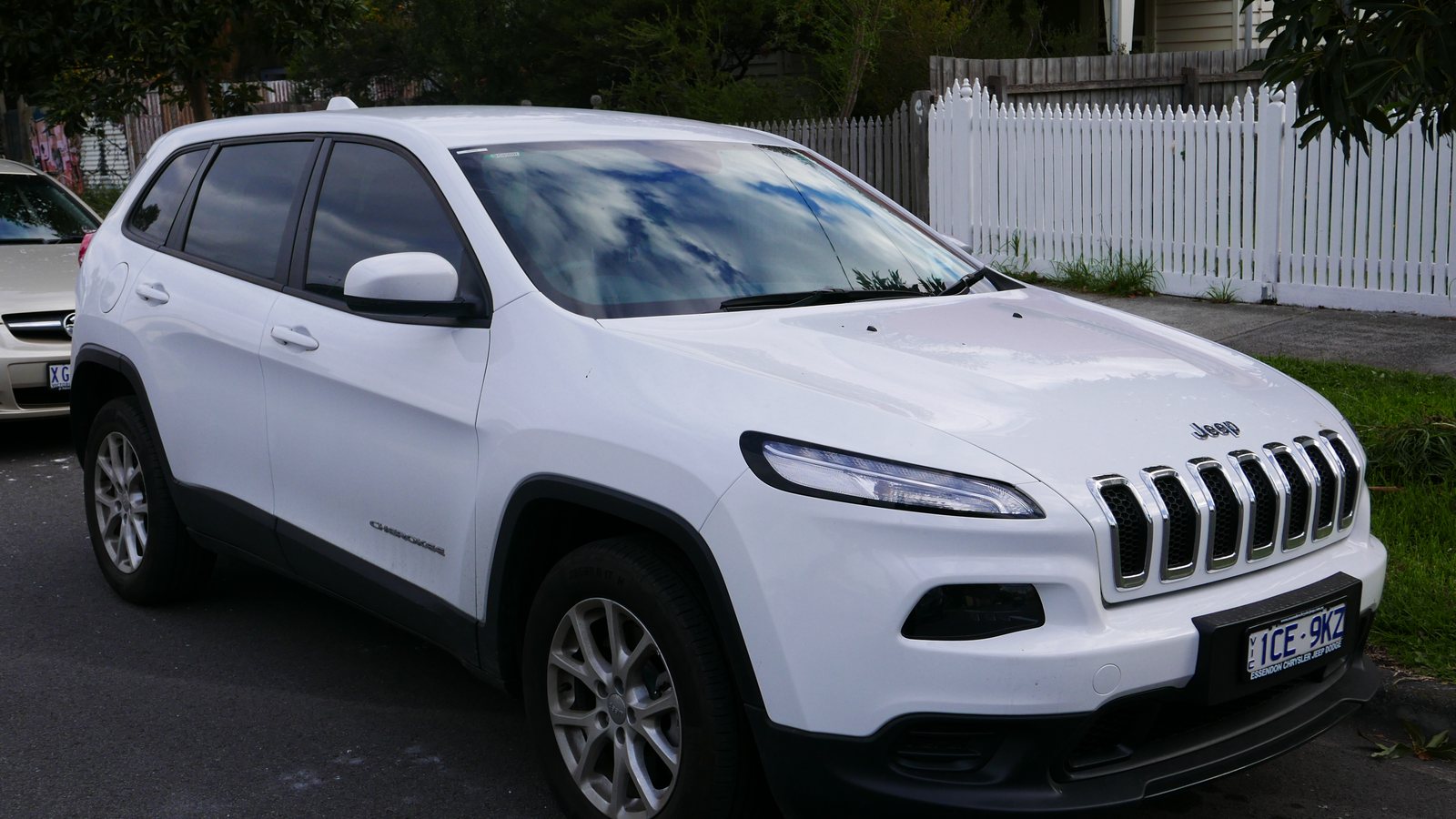 A white 2014 Jeep Cherokee parked on a residential street in front of a picket fence
