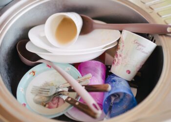Dirty plates, cups and cutlery piled in a stainless steel kitchen sink