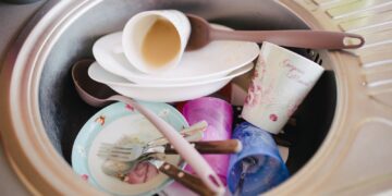 Dirty plates, cups and cutlery piled in a stainless steel kitchen sink