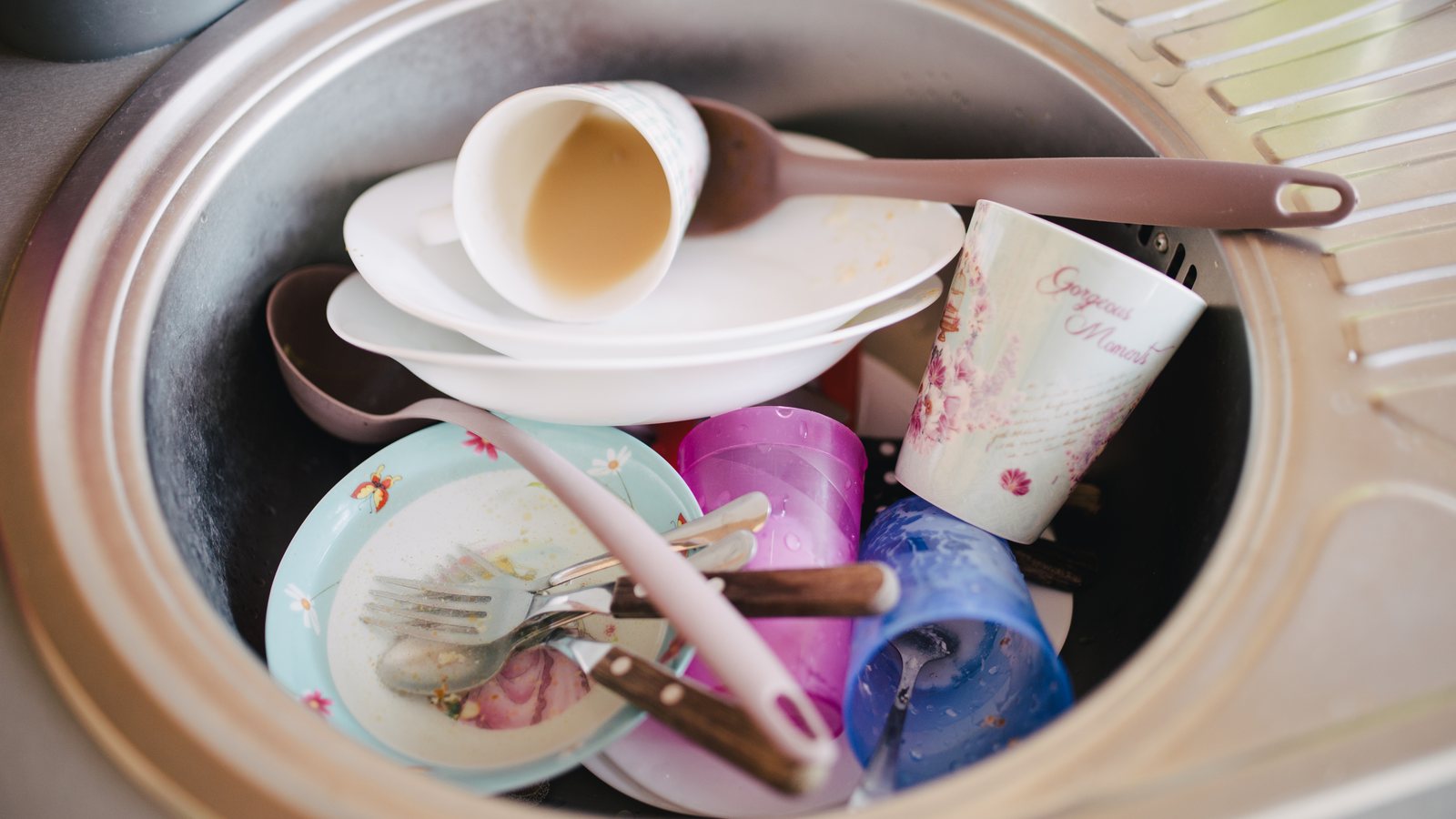 Dirty plates, cups and cutlery piled in a stainless steel kitchen sink