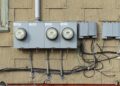 Three residential electric meters mounted on the shingled wall of a house