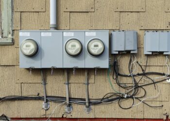 Three residential electric meters mounted on the shingled wall of a house