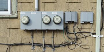 Three residential electric meters mounted on the shingled wall of a house