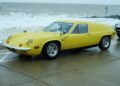 A yellow 1970 Lotus Europa parked on a wet seafront road in Felixstowe, England