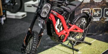 A red Sur-Ron electric dirt bike with foot pegs and no pedals on display at a trade show