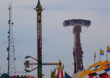 Traveling fair rides, including a tall drop tower and a spinning arm ride, on the midway at the Wisconsin State Fair