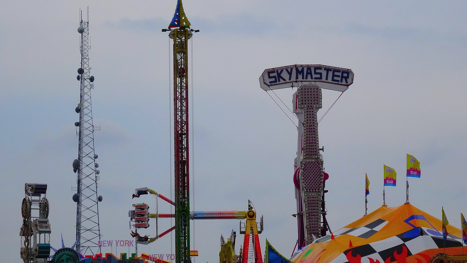 Traveling fair rides, including a tall drop tower and a spinning arm ride, on the midway at the Wisconsin State Fair