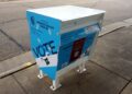 A blue and white official absentee ballot drop box marked Vote on a sidewalk in Madison, Wisconsin