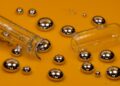 Silvery droplets of liquid mercury and a broken glass thermometer on an orange-gold surface