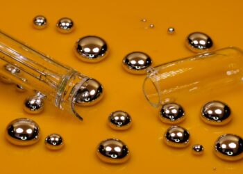 Silvery droplets of liquid mercury and a broken glass thermometer on an orange-gold surface