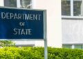Blue Department of State sign outside the Harry S. Truman Building in Washington, with hedges in front